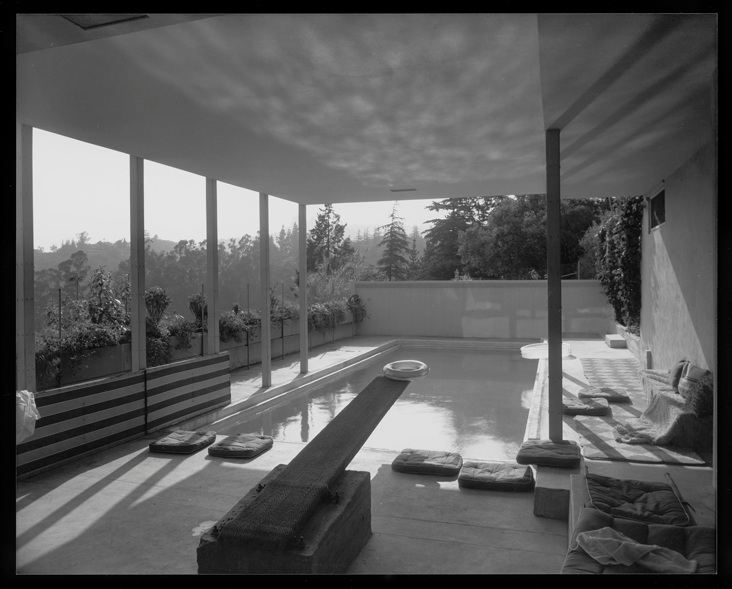 black and white interior photo of a house with floor to ceiling allowing sun rays to seep into the room